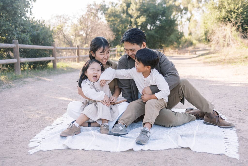 Asian family laughing and playing on a picnic blanket at a park in Orange County