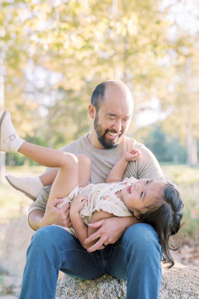 father holding laughing daughter in outdoor photoshoot location in Orange County