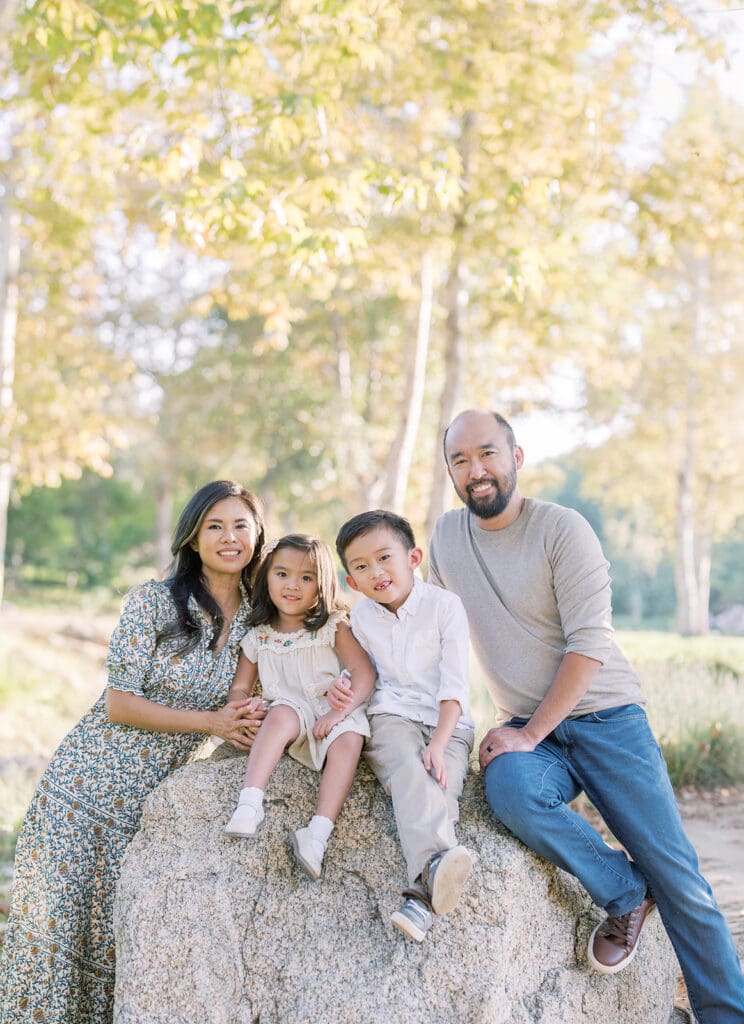 Family sitting and smiling on rock at outdoor photoshoot location in Orange County